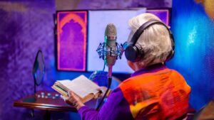 Tekoälyllä luotu psykedeelinen valokuva mummosta joka on kuulokkeet päässä lukemassa satuja mikrofoniin värikkäässä studiossa.