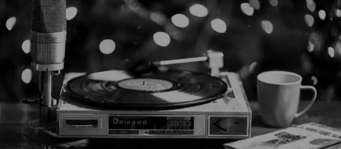 Tekoälyllä luotu mustavalko/sanomalehtikuva, jossa pöytämikrofoni, levysoitin, kahvikuppi ja kirja puisella tasolla.