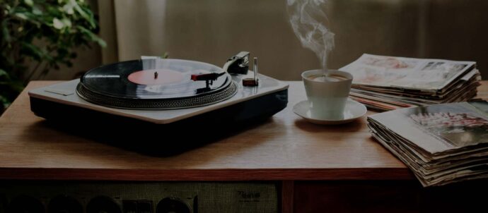 Tekoälyllä luotu rakeinen valokuva, jossa levysoitin, höyryävä kahvikuppi ja aikakausilehtiä puupintaisen radion päällä.