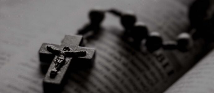 Rakeinen, mustavalkoinen lähikuva avonaisen raamatun päälle asetellusta krusifiksistä.