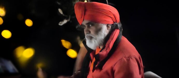 Kuva punaisiin vaatteisiin ja päähineeseen pukeutuneesta toimittajasta katsomassa kameran ohi.