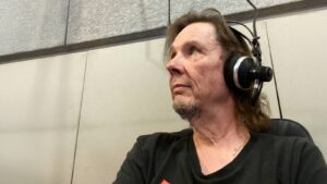 Radiotoimittaja studiossa, kuulokkeet päässään, katsoo kuvassa oikealle yläviistoon.